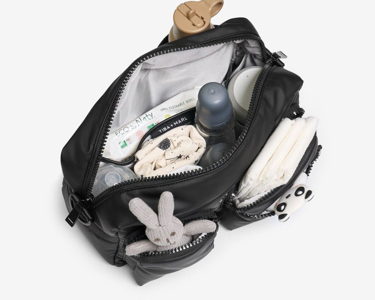 Open black backpack with baby items including a bottle, toys, and diapers on a white background