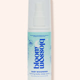 A bottle of Blossom & Soho Baby Whisperer calming baby sleep spray, featuring a white and light blue design with a white spray cap, set against a solid pale peach background.