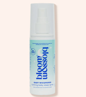 A bottle of Blossom & Soho Baby Whisperer calming baby sleep spray, featuring a white and light blue design with a white spray cap, set against a solid pale peach background.