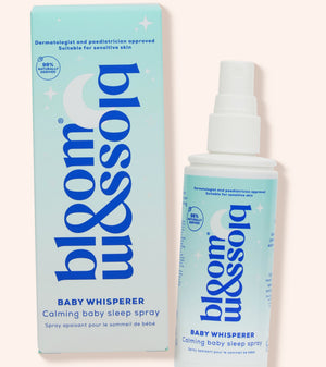 Blossom & Soho Baby Whisperer calming baby sleep spray shown with its light blue and white packaging box and spray bottle on a pale pink background.