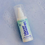 A bottle of bloom babywhisperer baby shower spray with a white pump and a light blue-green label, shown on a textured light blue background.