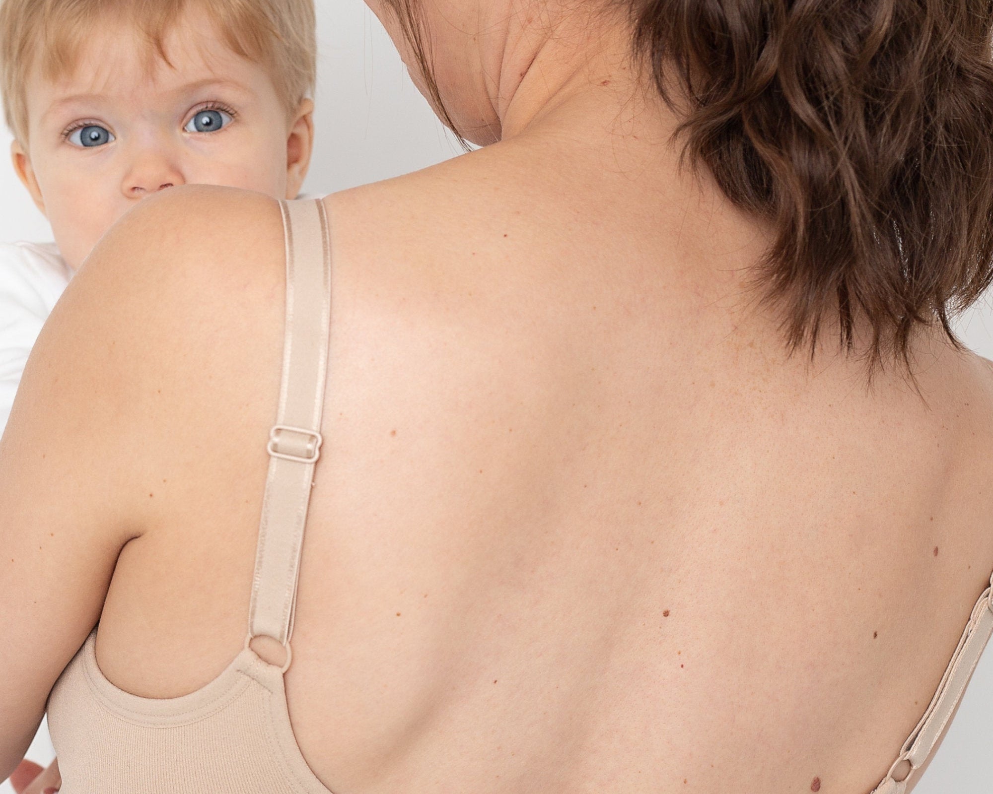 Woman wearing a beige compression garment with a baby peeking from behind.