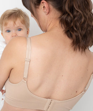 Woman wearing a beige compression garment with a baby peeking from behind.