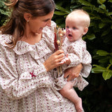 Beatrice Rose Stripe nightie worn by a woman holding a baby in a matching outfit and dried flowers by a hedge