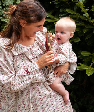 Beatrice Rose Stripe nightie worn by a woman holding a baby in a matching outfit and dried flowers by a hedge