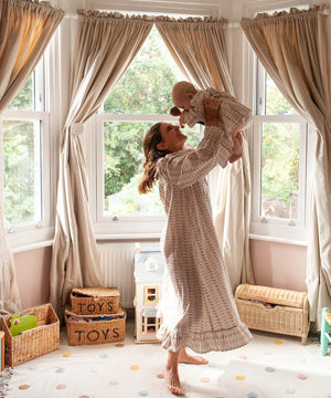 Beatrice Rose Stripe nightie worn by a woman lifting a smiling baby overhead in a bright bay-windowed nursery