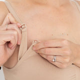 Person adjusting a beige bra strap on a plain background