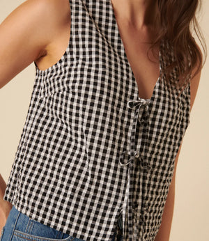 Black and white checkered sleeveless top worn by a person on a beige background