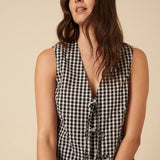 Woman wearing a black and white checkered sleeveless top against a beige background