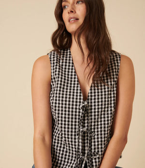 Woman wearing a black and white checkered sleeveless top against a beige background