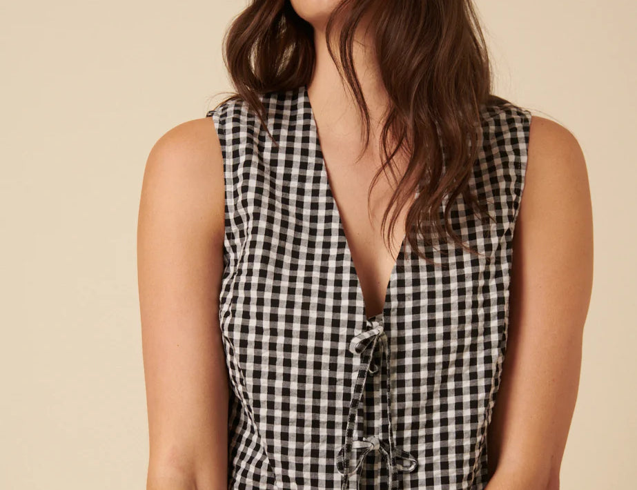 Woman wearing a black and white checkered sleeveless top against a beige background