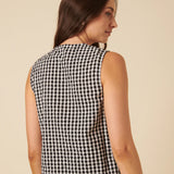 Woman wearing a black and white checkered sleeveless top against a beige background
