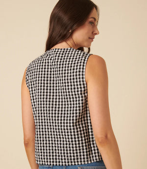 Woman wearing a black and white checkered sleeveless top against a beige background