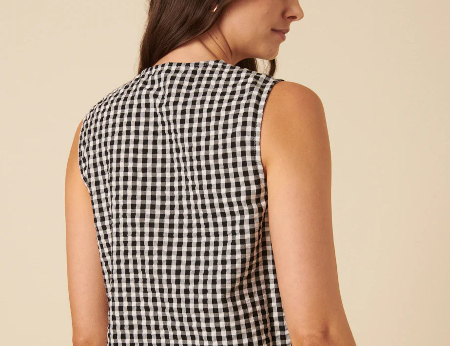 Woman wearing a black and white checkered sleeveless top against a beige background