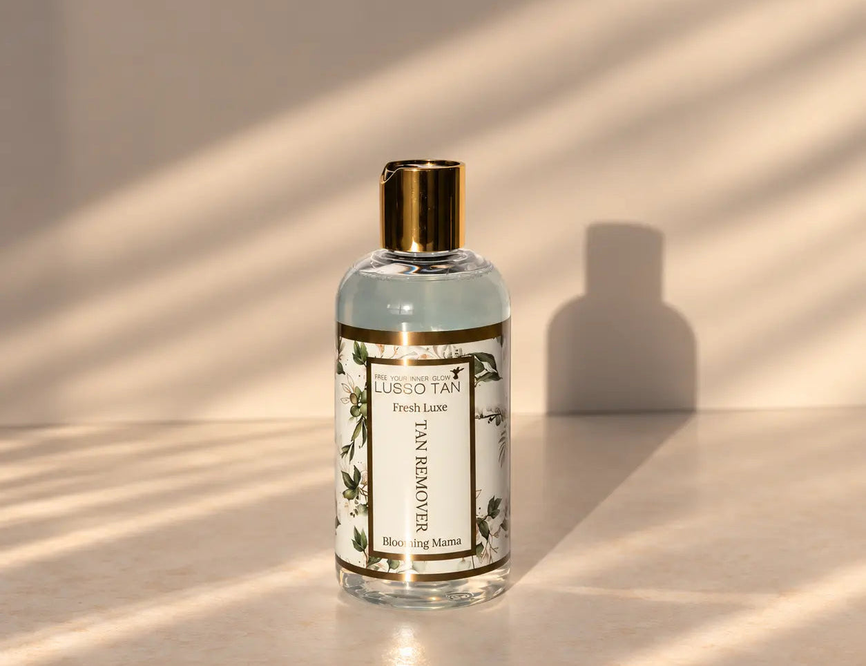 Fresh Lux Tan Removing Shower Gel bottle with gold cap in streaks of sunlight on a pale surface, casting a shadow