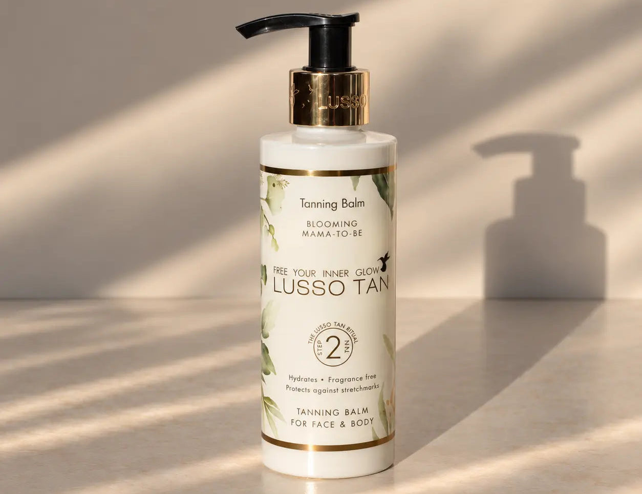 Blooming Mama To Be Tanning Balm standing upright with pump top, casting a shadow in soft sunlight on a cream surface