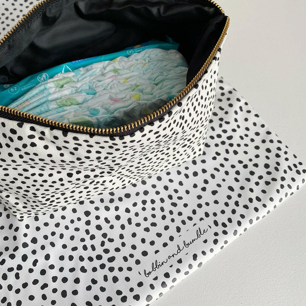 Nappy wallet in dalmatian print, open at an angle showing nappies and wipes inside, with the mat beneath