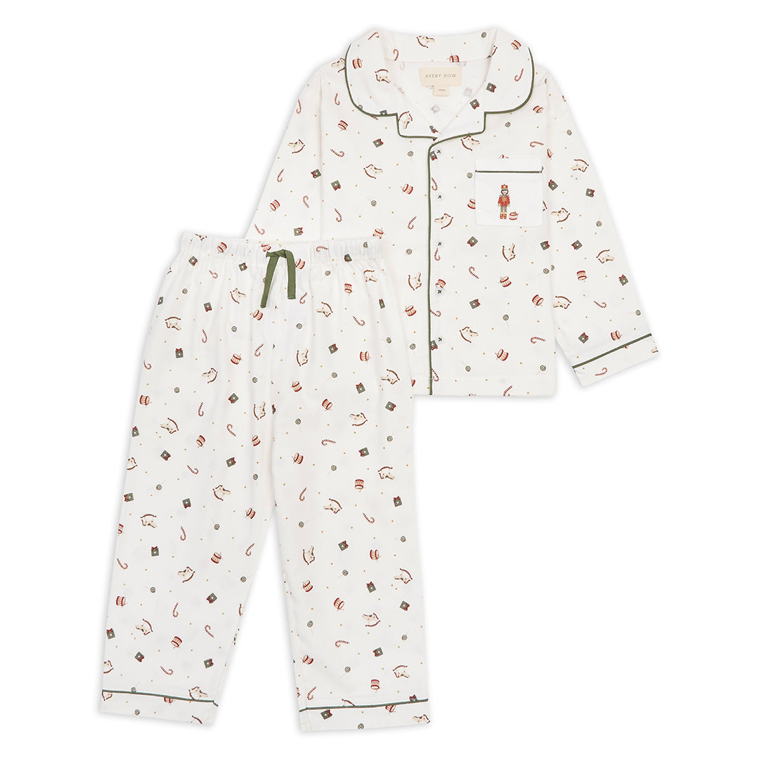 A two-piece children's pajama set featuring a long-sleeve button-front top and matching pants. The pajamas are off-white with a small all-over print of red, brown, and dark green candy and gift motifs, accented with dark green piping and a green drawstring.
