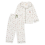 A two-piece children's pajama set featuring a long-sleeve button-front top and matching pants. The pajamas are off-white with a small all-over print of red, brown, and dark green candy and gift motifs, accented with dark green piping and a green drawstring.