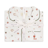 A folded white pajama set with a festive holiday print, tied with a white ribbon printed with the brand name 'Avery Row'. The pajamas feature a pattern of red and gold ornaments, candy canes, and a small nutcracker on the pocket, with dark green piping.