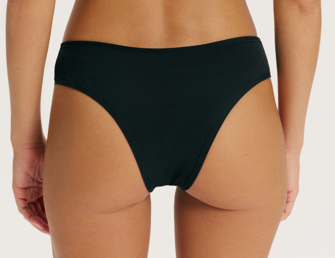 Rear view of a model wearing a solid black bikini bottom against a clean, light off-white background.