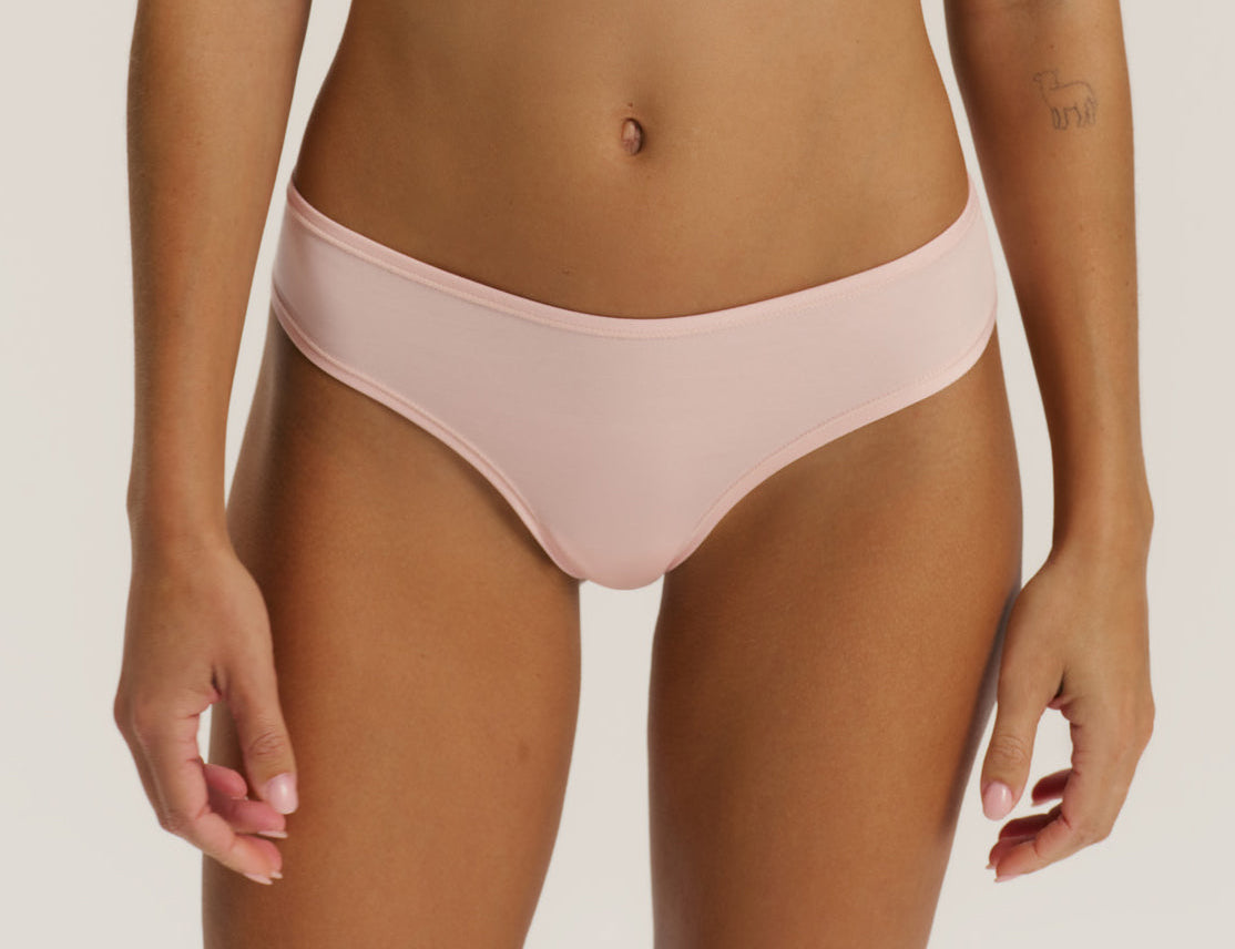 A model wearing a light pink, low-rise bikini bottom against a plain light beige background.
