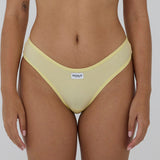 A close-up of a model wearing a pale yellow ribbed bikini bottom with a white brand label reading 'RENUE' on the front, set against a plain light gray background.