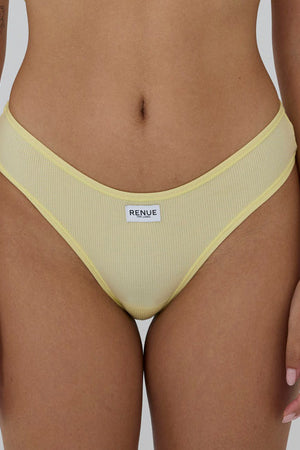 A close-up of a model wearing a pale yellow ribbed bikini bottom with a white brand label reading 'RENUE' on the front, set against a plain light gray background.