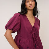 Woman wearing a burgundy blouse with puff sleeves against a plain background