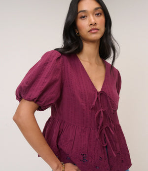 Woman wearing a burgundy blouse with puff sleeves against a plain background