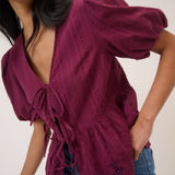 Woman wearing a burgundy open-knit cardigan over a black top with blue jeans on a plain background