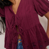 Close-up of a person wearing a burgundy top with ruffled layers and blue jeans.