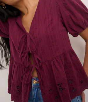Close-up of a person wearing a burgundy top with ruffled layers and blue jeans.