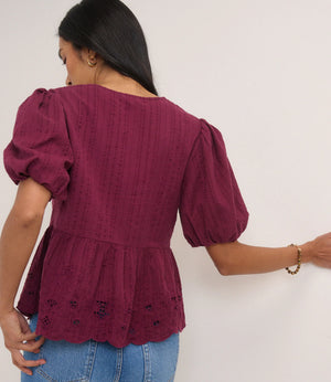 Woman wearing a burgundy top with puff sleeves against a white background