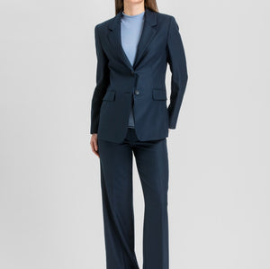 A woman modeling a navy blue two-piece suit with a light blue top and brown heels, standing against a light gray studio background.