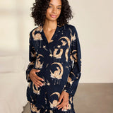 A woman modeling a navy blue pajama set with a celestial print of gold crescent moons, stars, and flowers, set against a neutral bedroom background.