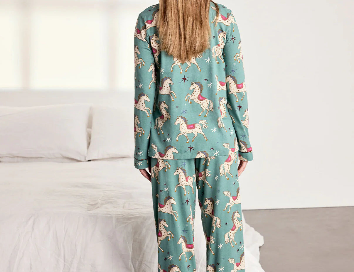 Woman wearing a teal pajama set with animal prints in a bedroom setting.