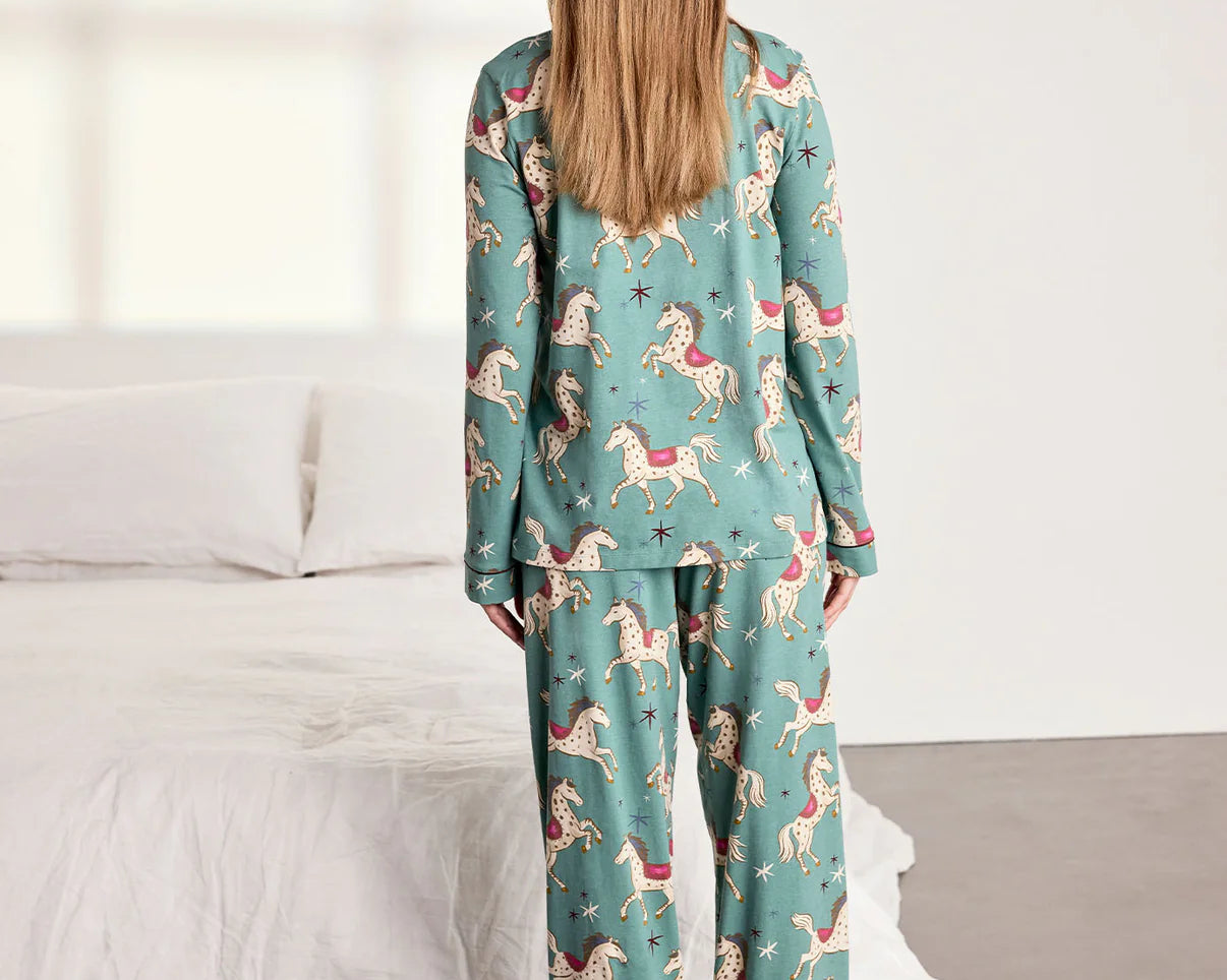 Woman wearing a teal pajama set with animal prints in a bedroom setting.