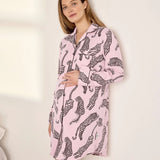 A woman wearing a pink long-sleeve pajama shirt with a black leopard print, standing against a plain off-white wall.