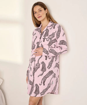 A woman wearing a pink long-sleeve pajama shirt with a black leopard print, standing against a plain off-white wall.