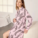 A woman wearing a pink long-sleeve pajama shirt dress with a black leopard print pattern, sitting on a white armchair in a bright bedroom setting.