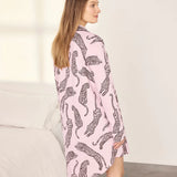 A woman wearing a pink long-sleeve shirt dress with a black leopard print pattern, standing in a brightly lit bedroom.