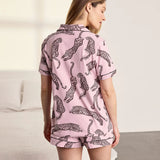 A woman wearing a light pink short-sleeve pajama set with a black leopard print, shown from the back in a bedroom setting.
