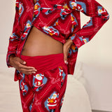 A person wearing a red pajama set with a festive Santa Claus print, photographed indoors against a light neutral bedroom background.