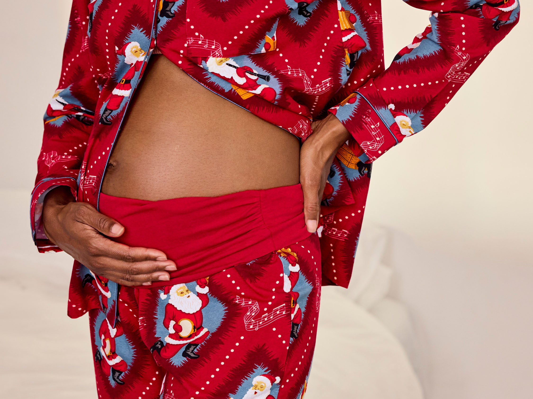 A person wearing a red pajama set with a festive Santa Claus print, photographed indoors against a light neutral bedroom background.