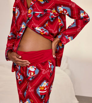 A person wearing a red pajama set with a festive Santa Claus print, photographed indoors against a light neutral bedroom background.
