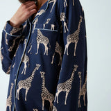 A close-up of a person wearing a navy blue pajama shirt with an all-over beige giraffe print and white piping details.