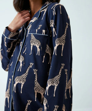 A close-up of a person wearing a navy blue pajama shirt with an all-over beige giraffe print and white piping details.