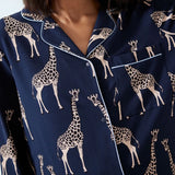 A close-up of a person wearing navy blue pajama top with a beige giraffe print and white piping trim.