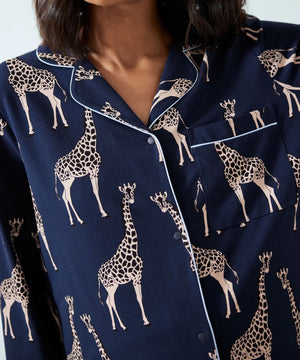 A close-up of a person wearing navy blue pajama top with a beige giraffe print and white piping trim.